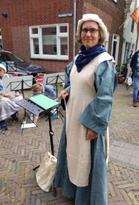 Wendolien staat in middeleeuwse kledij en een dirigeerstok te poseren vanachter haar lessenaar.